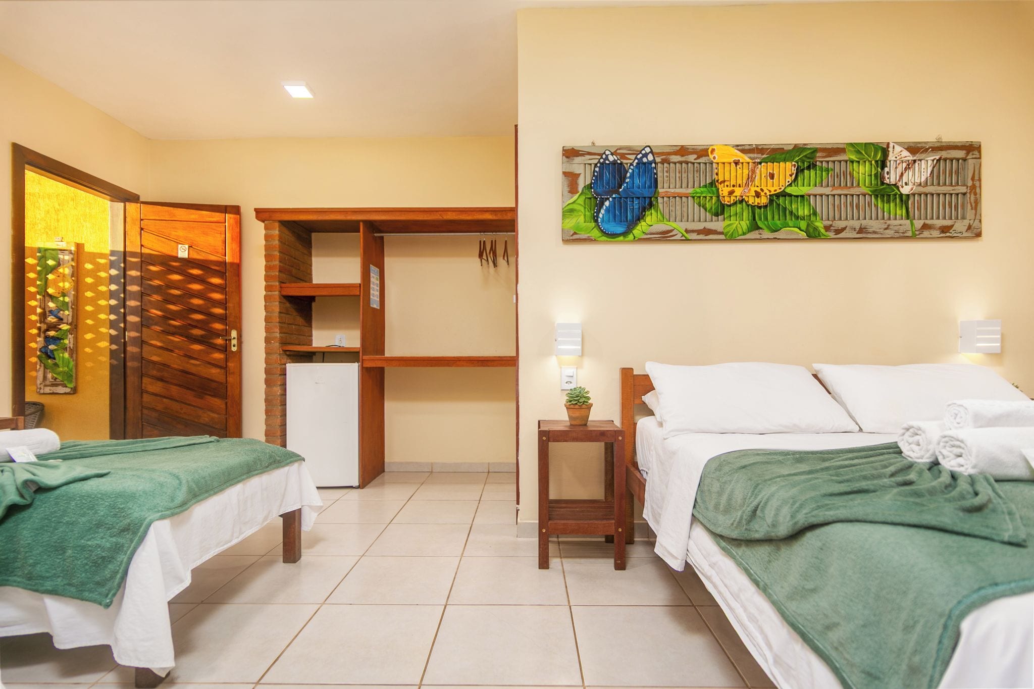 Habitación de hotel con dos camas, una mesita, una obra de arte colgada en la pared y una puerta con marco de madera.