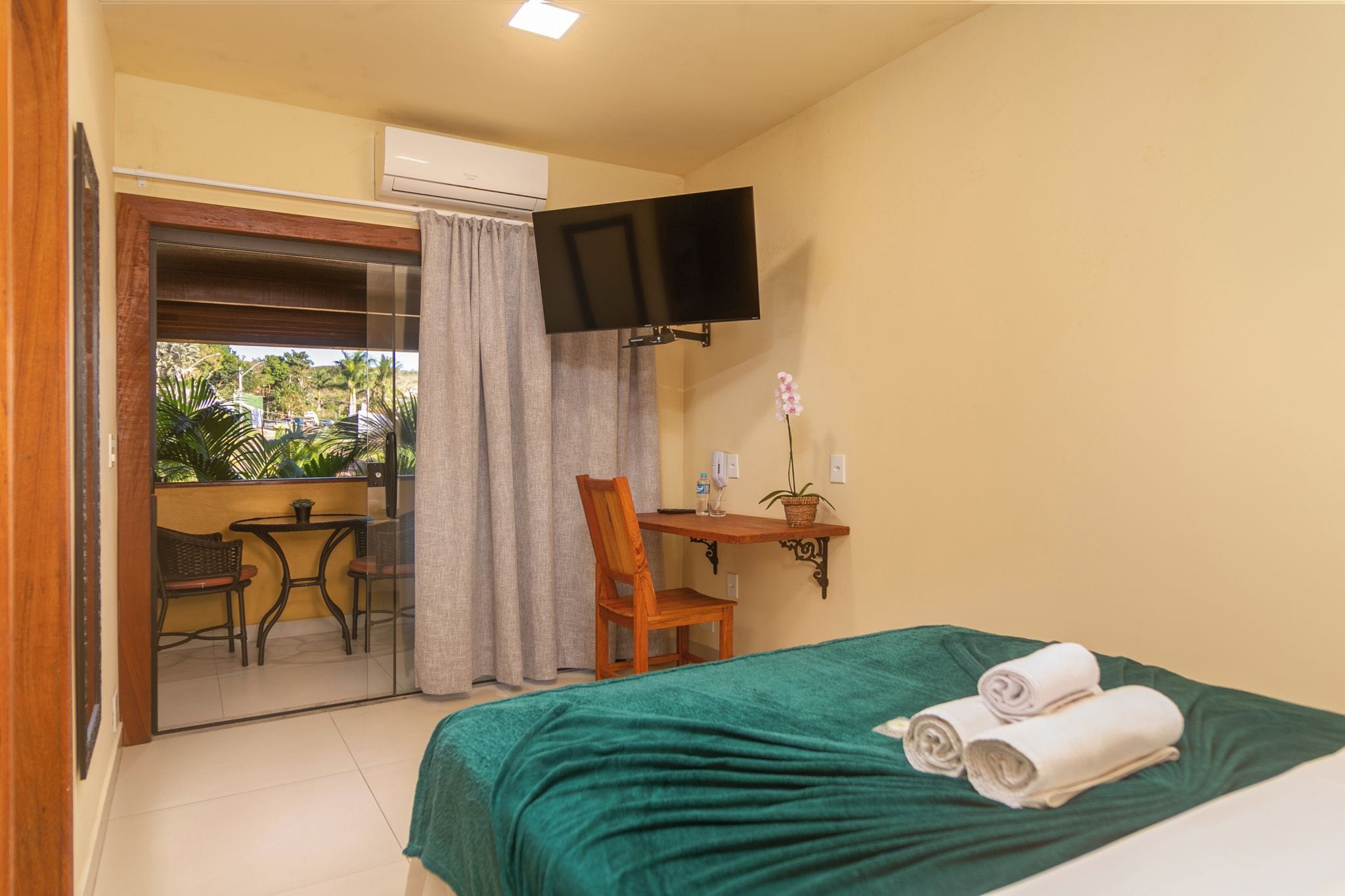A hotel room with a bed, a desk, a chair, a television, and a sliding glass door leading to an outdoor area.