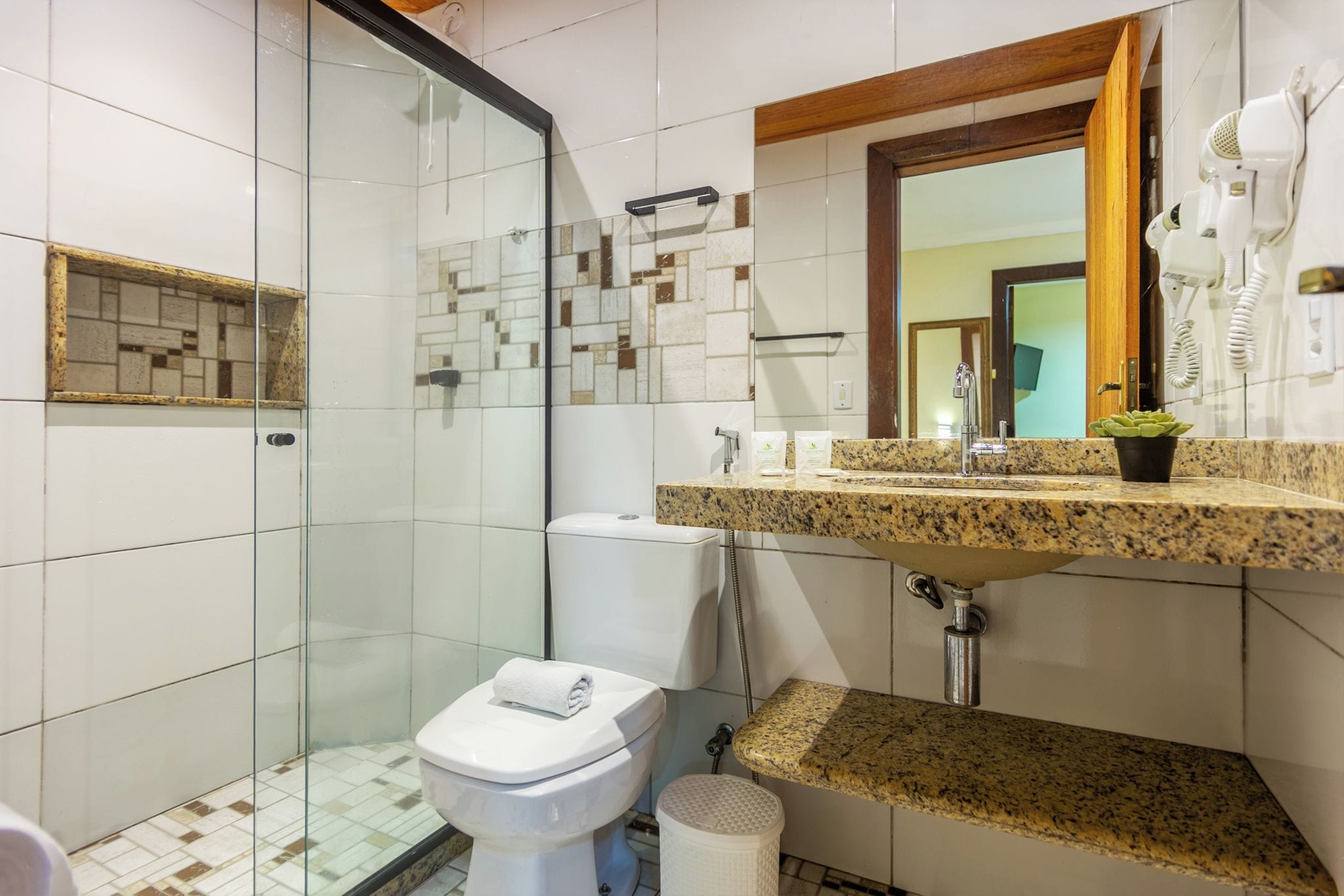 A bathroom with a glass shower enclosure, a white toilet, a granite countertop sink, and a mirror above the sink.