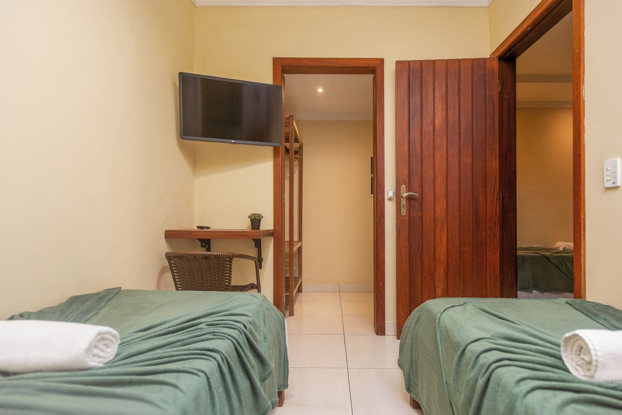 A hotel room with two beds, a TV, a small table with a plant, and a wooden door leading to another room.