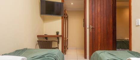 A hotel room with two beds, a TV, a small table with a plant, and a wooden door leading to another room.
