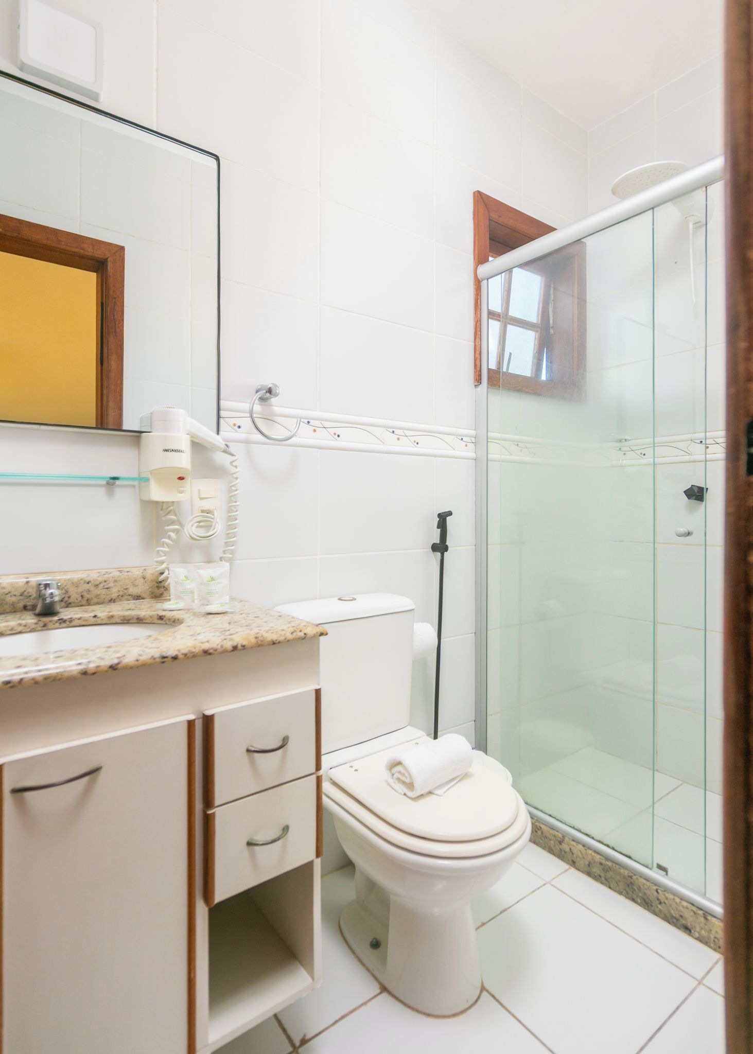 Un baño con inodoro, lavamanos con encimera de mármol, cabina de ducha de vidrio y espejo con marco de madera.