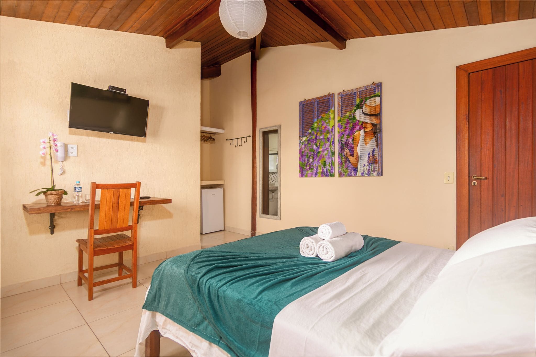 A hotel room with a bed, a desk with a chair, a television, and a painting on the wall.