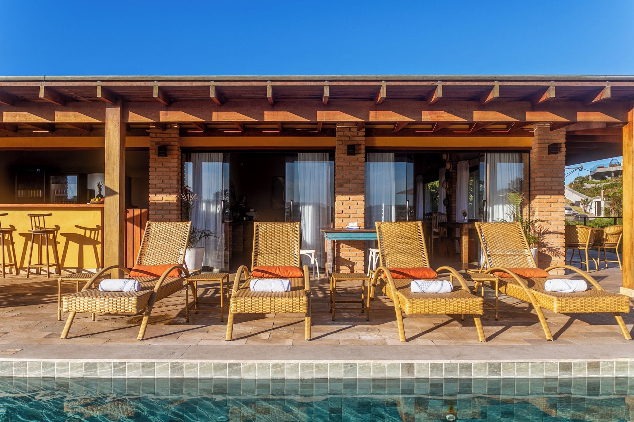 A poolside area with wicker lounge chairs and a table, a bar area with a counter, and a brick wall.