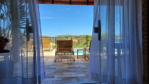 An open doorway leading to a patio with a pool, wicker chairs, and a view of a hilly landscape. - Pousada Búzios Garden (Búzios)