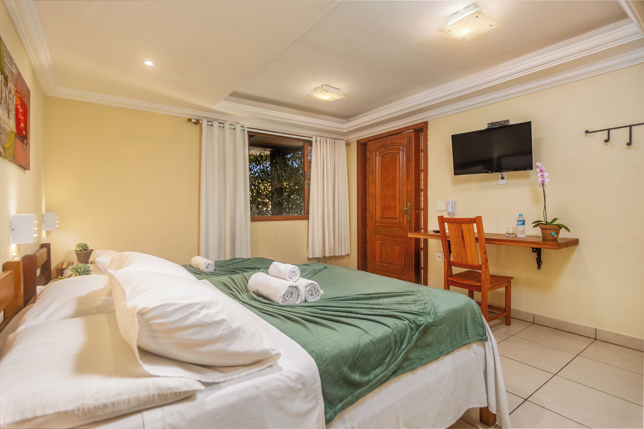 A hotel room with a bed, a desk, a television, and a window with curtains.