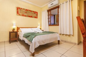 Une chambre d’hôtel avec un lit, une table de chevet avec une lampe, une fenêtre avec des rideaux et un climatiseur fixé au mur.