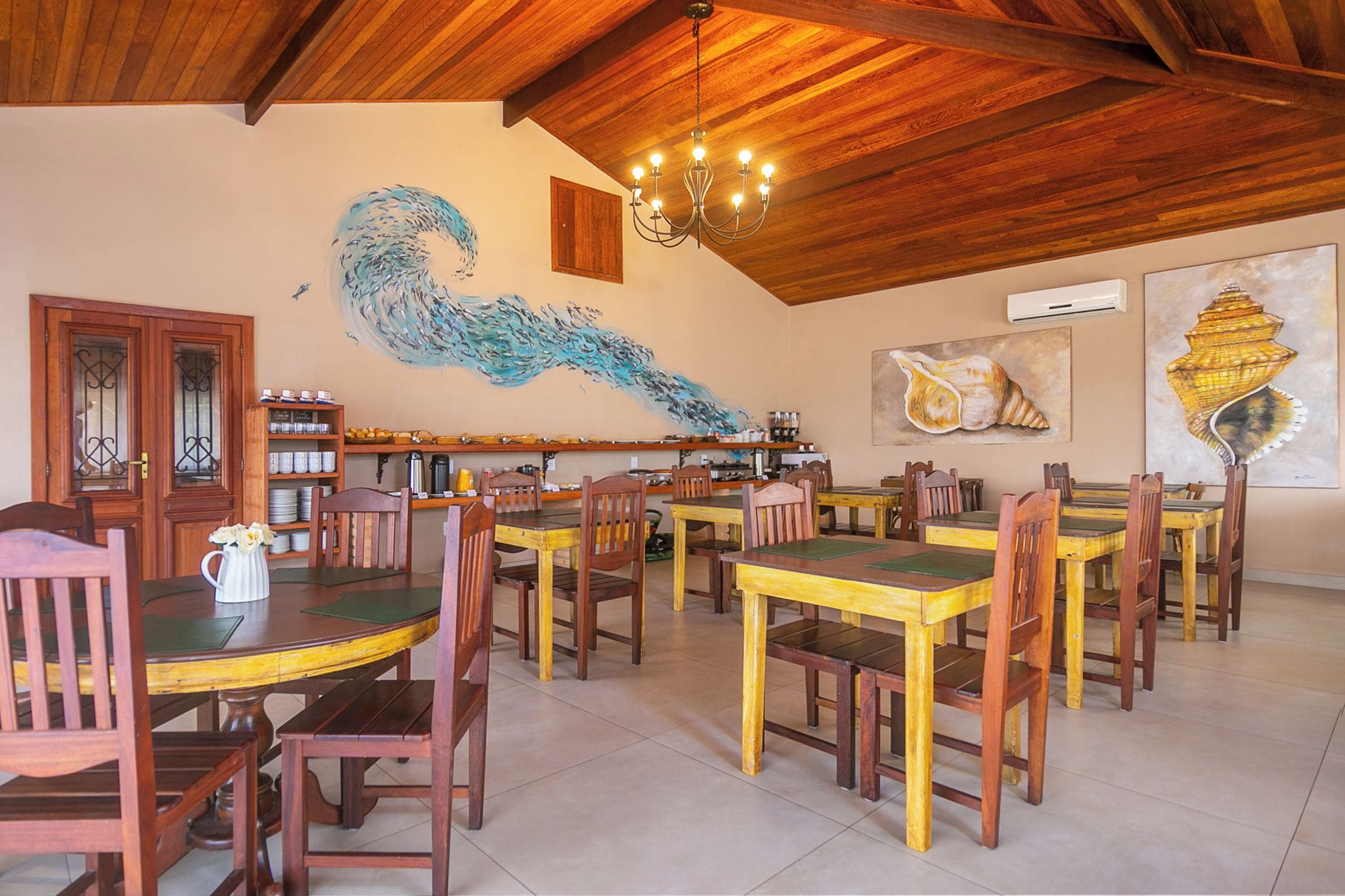 Un comedor con mesas y sillas de madera, un gran mural de un pez y una araña.
