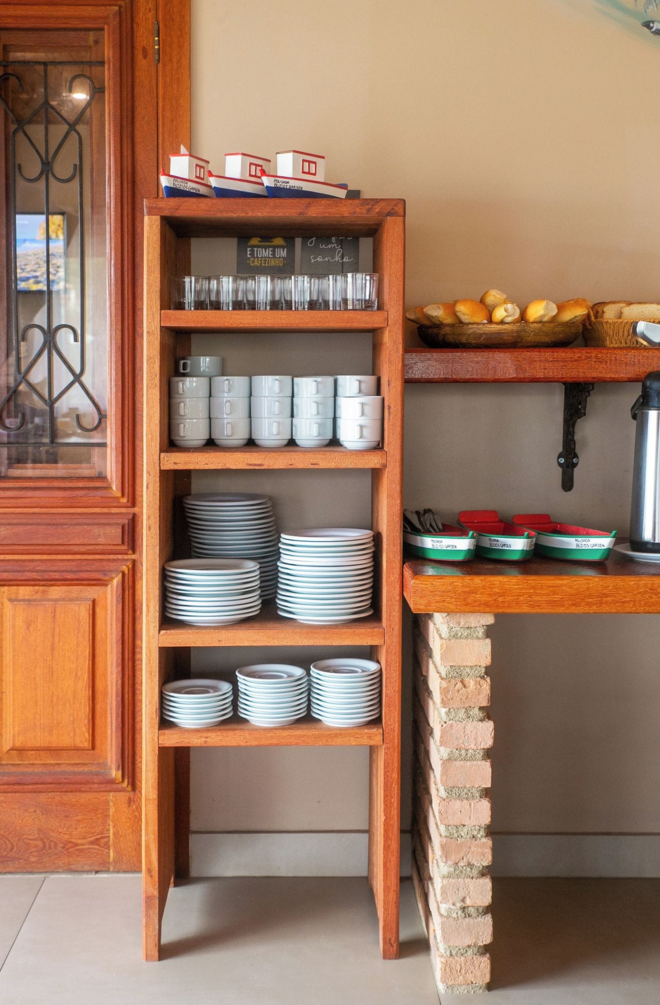 A kitchen with a wooden shelf holding plates, jars, and a coffee machine.