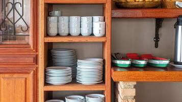 A kitchen with a wooden shelf holding plates, jars, and a coffee machine.