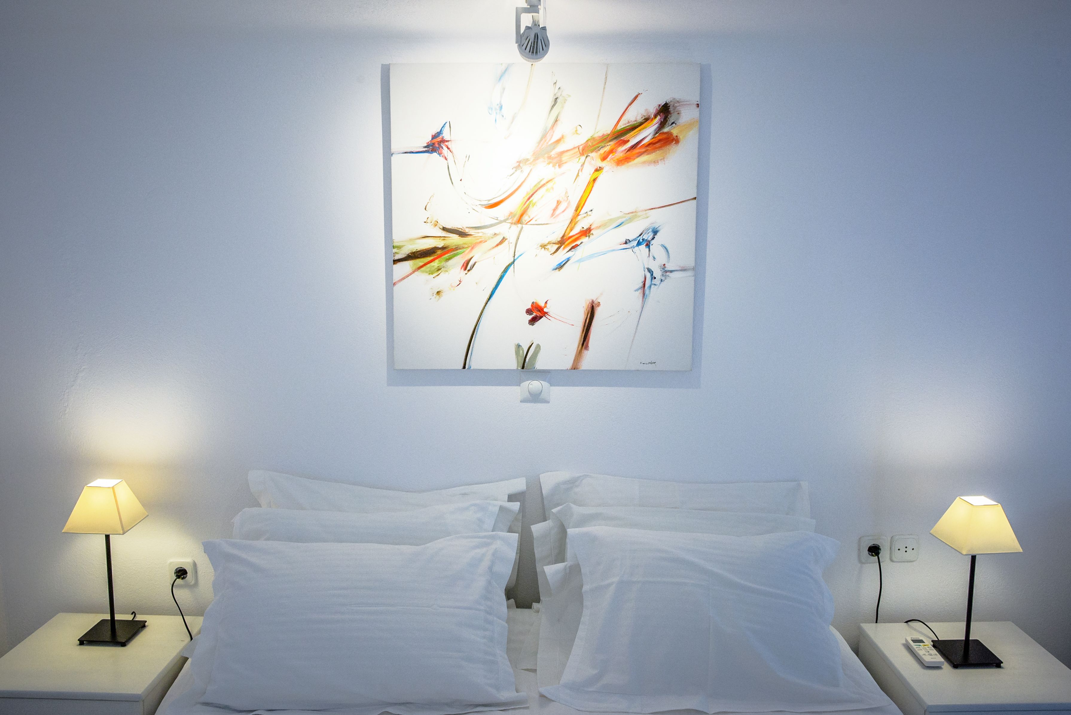 Een hotelkamer met een bed, twee nachtkastjes en een abstract schilderij aan de muur.