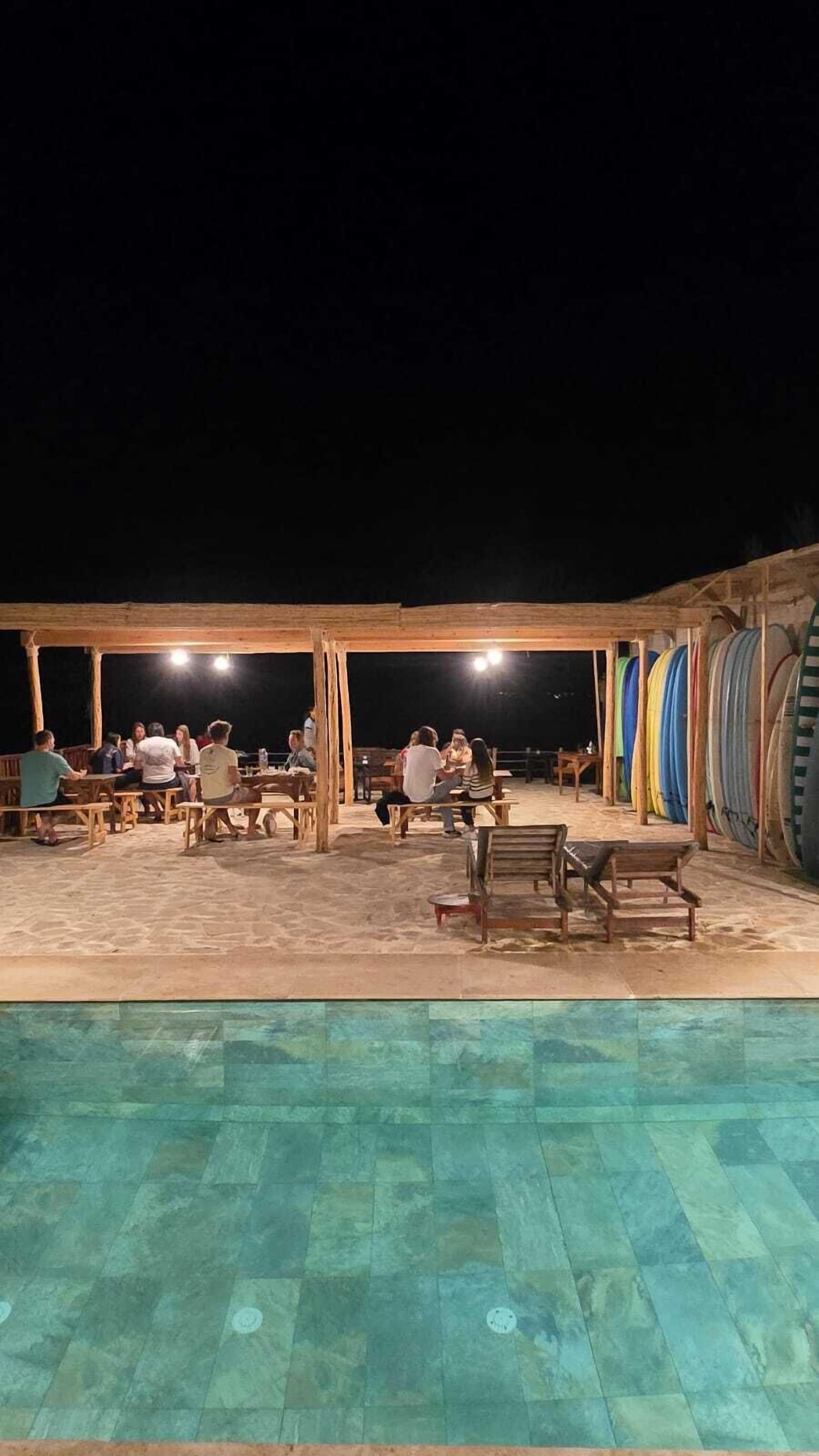 An outdoor pool area with wooden tables and benches, surrounded by a wooden pergola.
