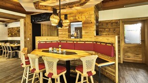 Un interior de madera con una mesa de comedor central, asientos tipo cabina tapizados en rojo y lámparas colgantes.