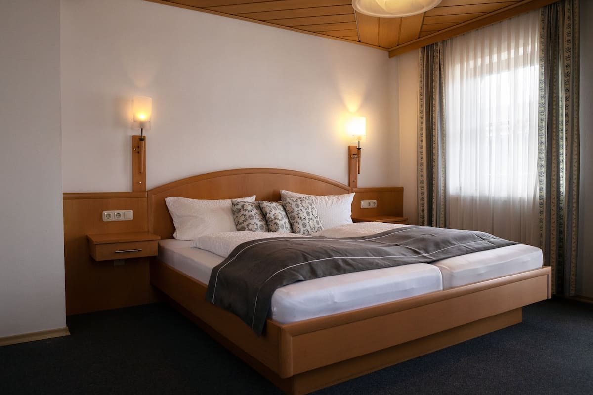 Un lit bien fait, avec une tête de lit en bois, deux tables de chevet avec des lampes et une fenêtre avec des rideaux.
