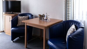 Una habitación con techo de madera, un televisor de pantalla plana sobre un mueble de madera, dos sofás de cuero azul con cojines estampados, una mesa de madera y un cuadro en la pared.