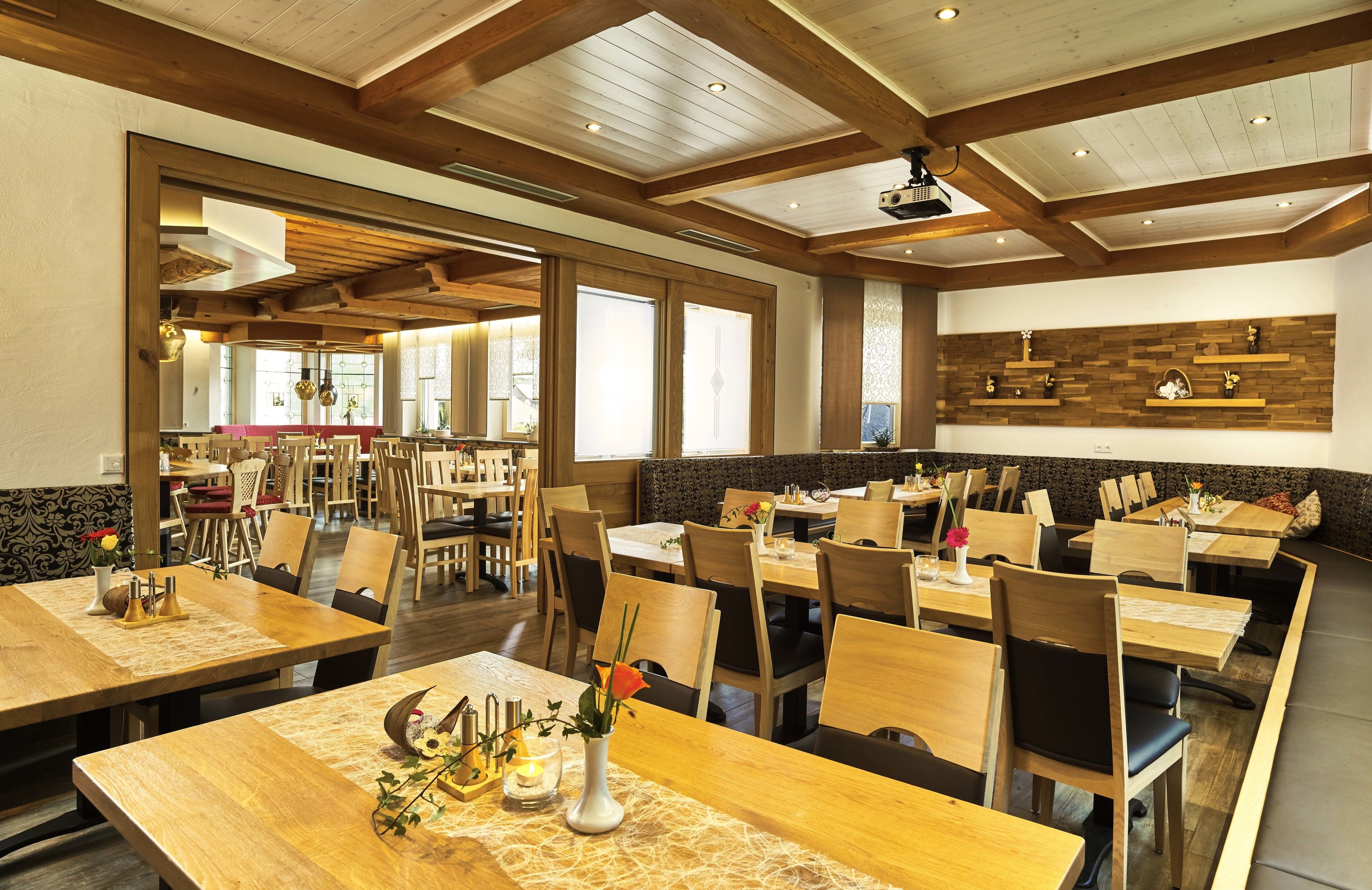 Ein geräumiges Restaurant mit Holztischen und -stühlen, einer hohen Decke mit sichtbaren Balken und einer Wand mit Backsteinverkleidung.