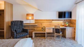 Una habitación de hotel con cama, escritorio, silla, televisor y lámpara.