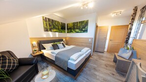 Un dormitorio moderno con una cama grande, un sofá, una mesita con vasos y suelo de madera.