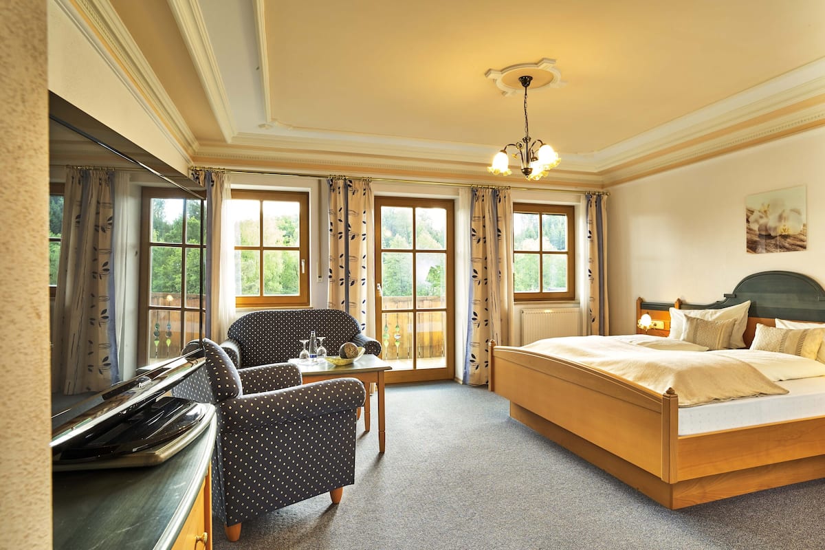 Une chambre à coucher avec un lit, un bureau et une chaise. Il y a des fenêtres avec des rideaux, un lustre et un tableau au mur.