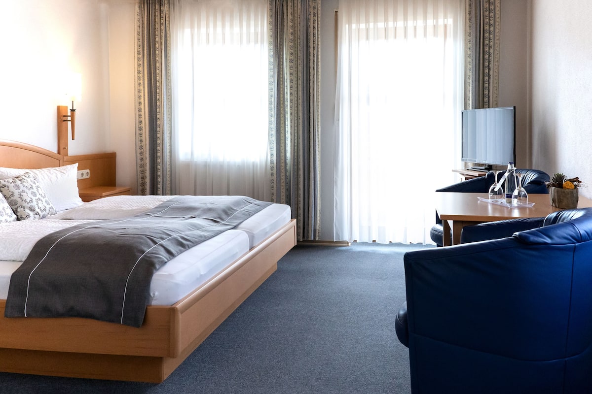 Une chambre d’hôtel avec un lit, un bureau doté d’une télévision et une chaise bleue.