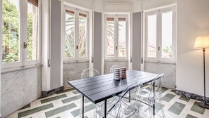 A dining area with a table and chairs, large windows with wooden shutters, and a floor with a geometric pattern. - AwesHome - Sea Sensation Apartment (La Spezia)