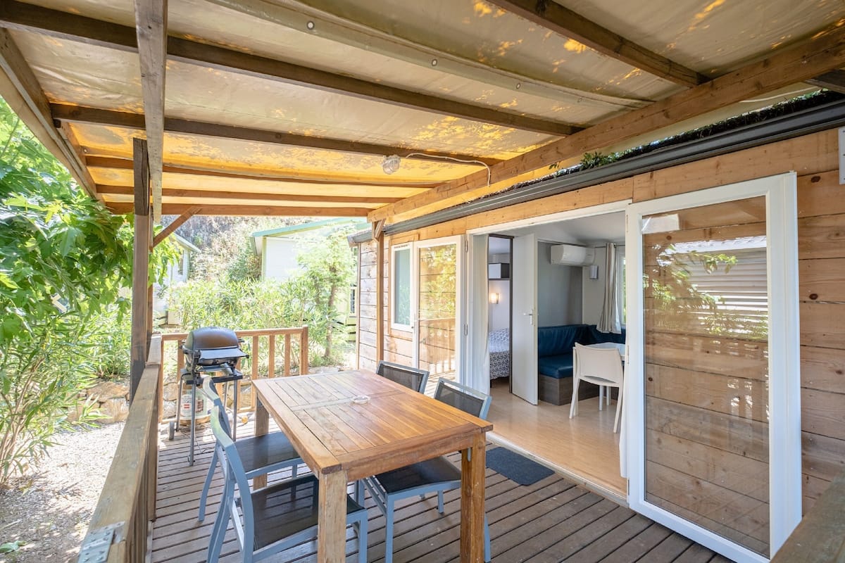 Una terraza de madera con mesa y sillas, una parrilla y un porche cubierto.