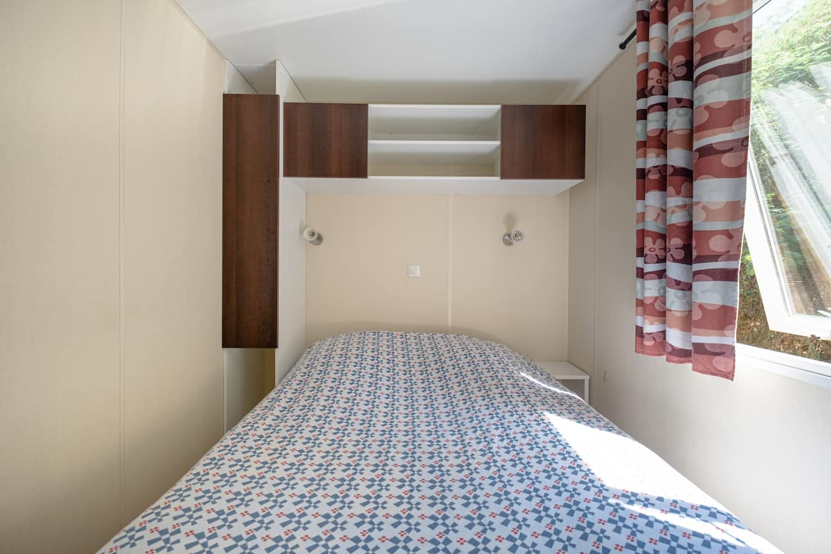 Un dormitorio con cama, una ventana con cortinas y armarios empotrados de madera sobre la cama.