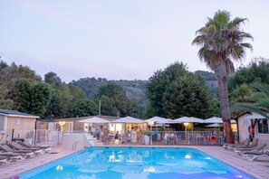 A swimming pool with lounge chairs and umbrellas, surrounded by buildings and trees. - Camping Parc des Monges (Auribeau-sur-Siagne)