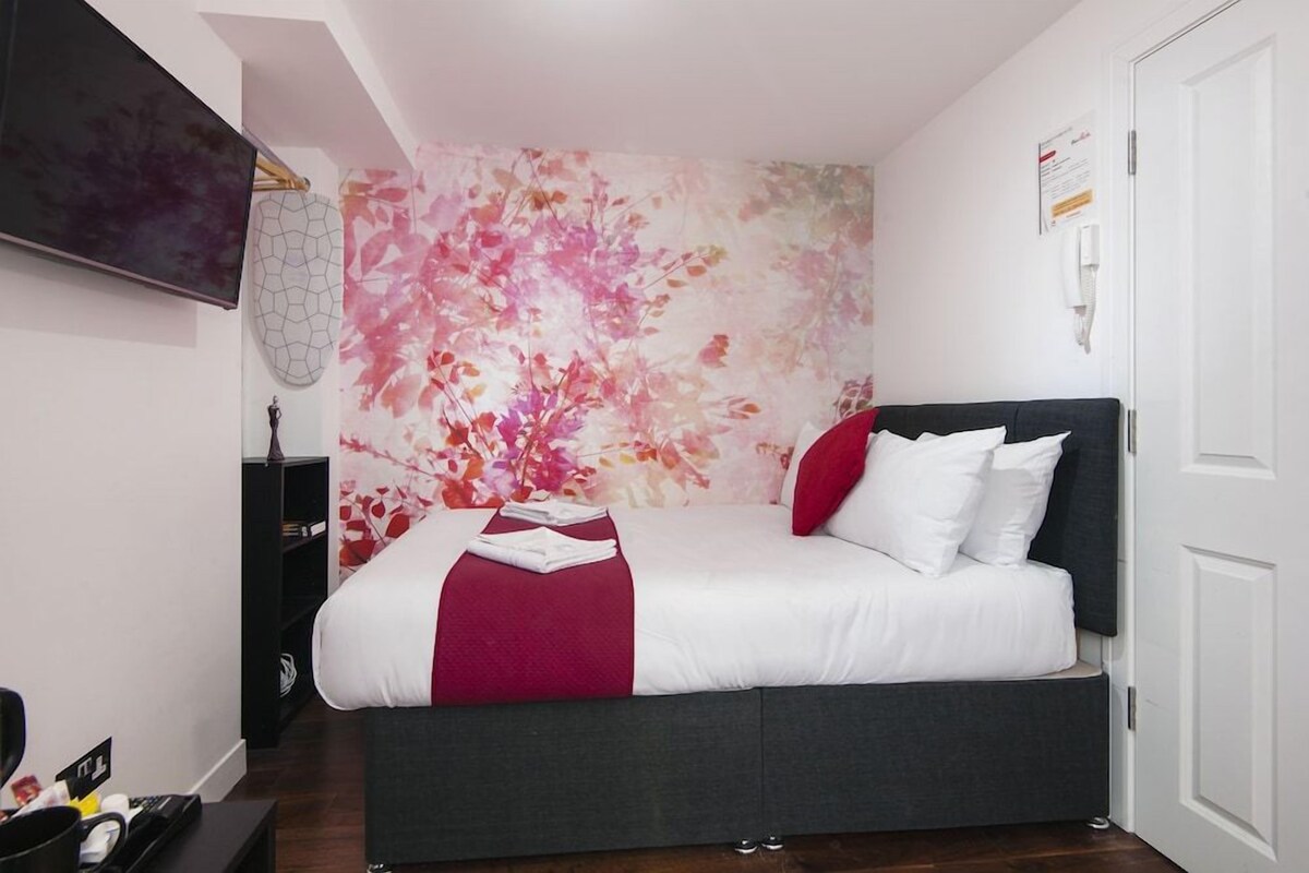 A modern bedroom with a bed, a wall tapestry, a flat-screen TV, and a door with a sign.