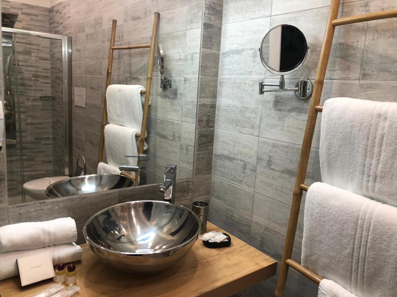 A modern bathroom with a large mirror, a wooden ladder, a sink with a large bowl, and neatly stacked towels.