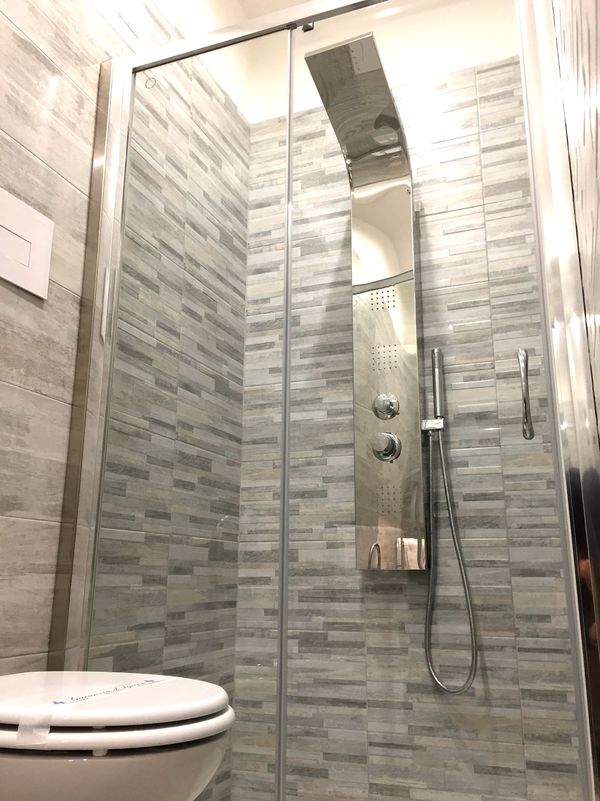 Une salle de bain moderne avec une douche à parois de verre, des toilettes et un mur carrelé.