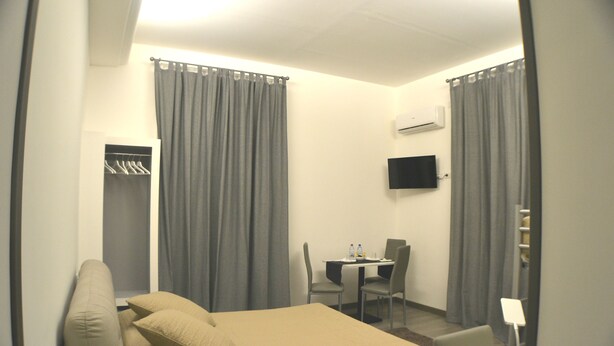 Habitación de hotel con cama, escritorio, sillas, televisor y armario.