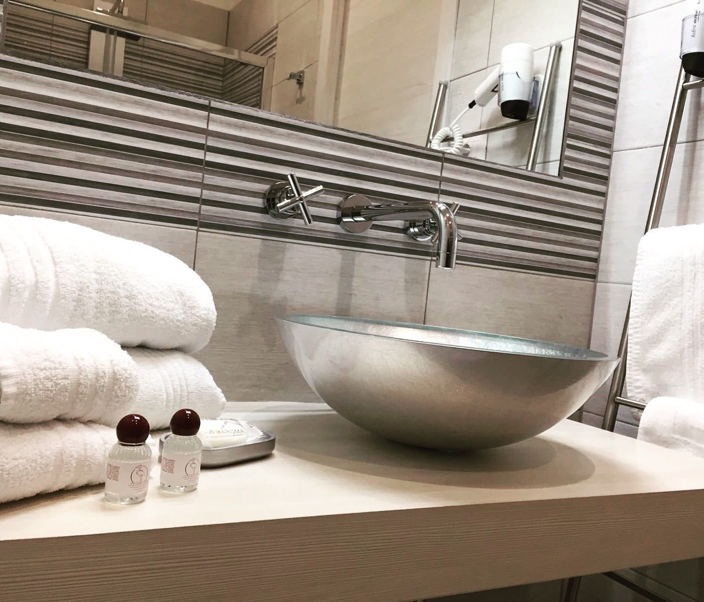 Ein modernes Badezimmer mit einem großen Glaswaschbecken, einem Handtuchhalter mit gefalteten Handtüchern und einem an der Wand befestigten Föhn.