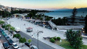 Un paseo marítimo con un amplio espacio para peatones, un quiosco central y vistas al mar y montañas a lo lejos.
