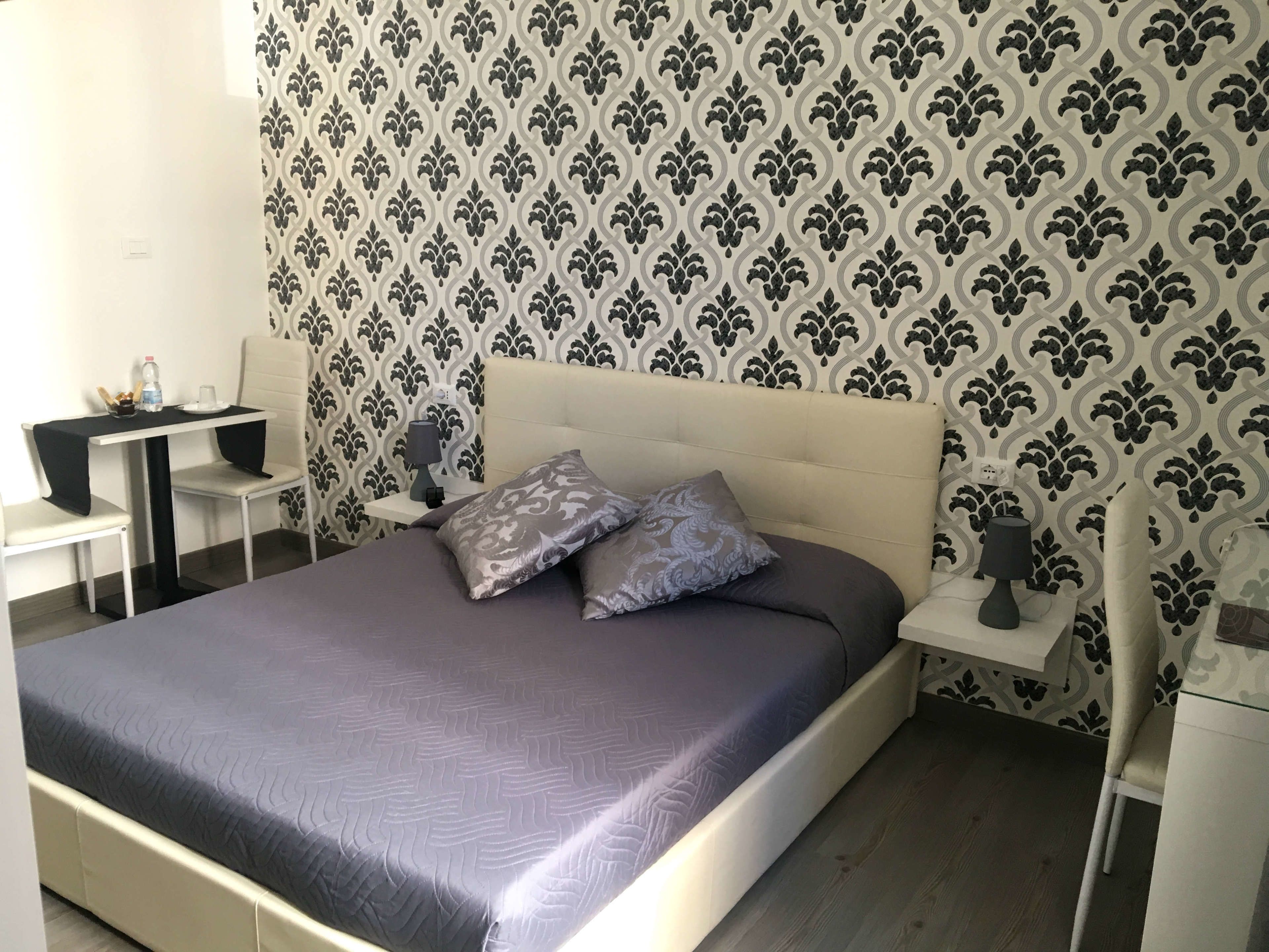 Un dormitorio ordenado con una cama, mesitas de noche y un escritorio pequeño con una silla.