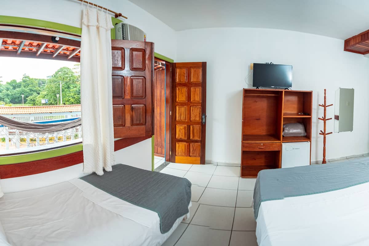 A hotel room with two beds, a TV, a wardrobe, and a view of a train station.