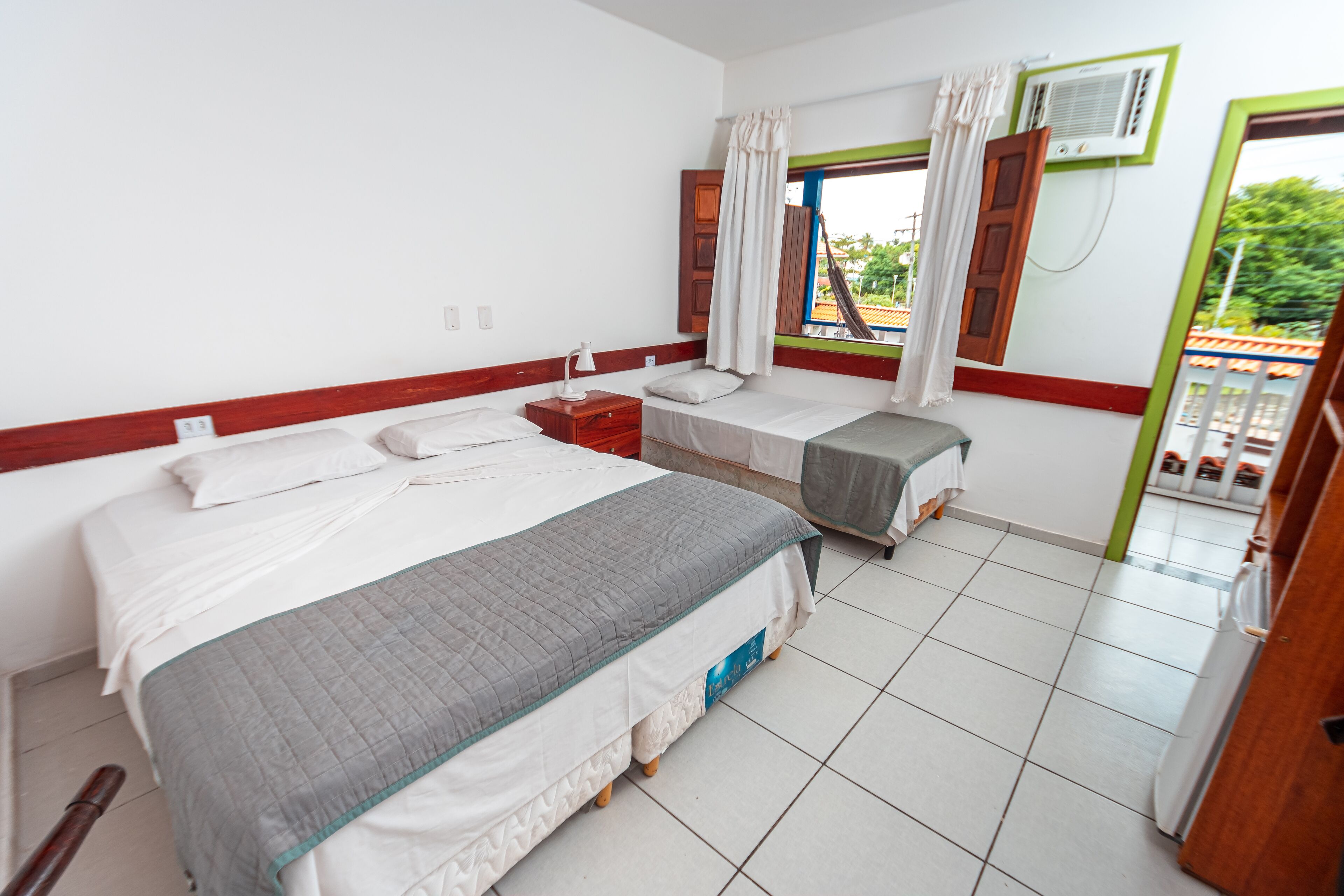 Ein Hotelzimmer mit einem großen Bett, einem kleineren Bett, einem Schreibtisch und einem Fenster mit Vorhängen.