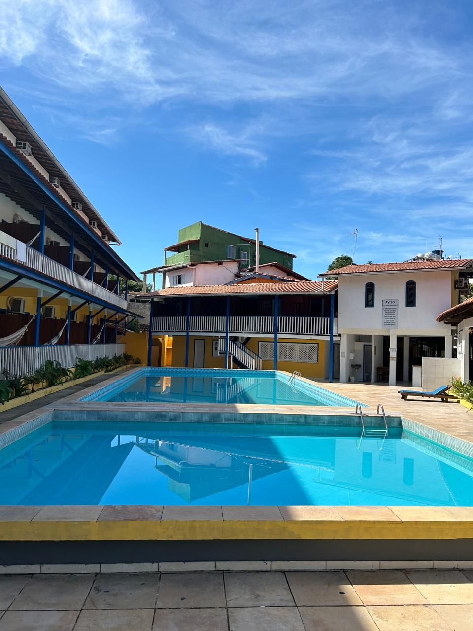 Una piscina con superficie de agua azul cristalina, rodeada de edificios con balcones y una zona cubierta.