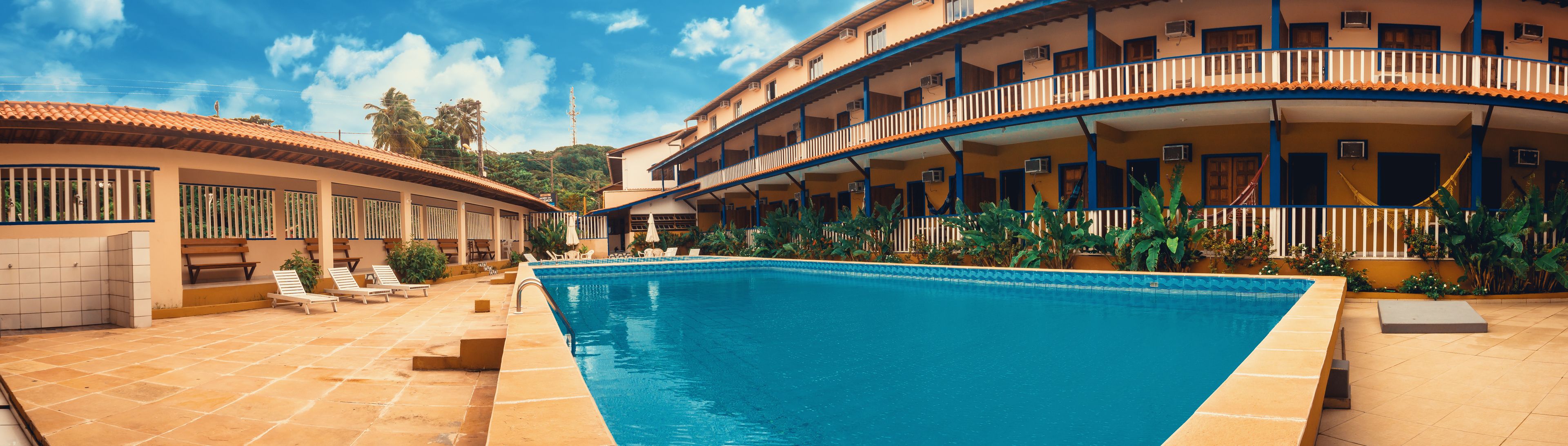 Un hotel con piscina, zona de estar al aire libre y un edificio de dos pisos con balcones.
