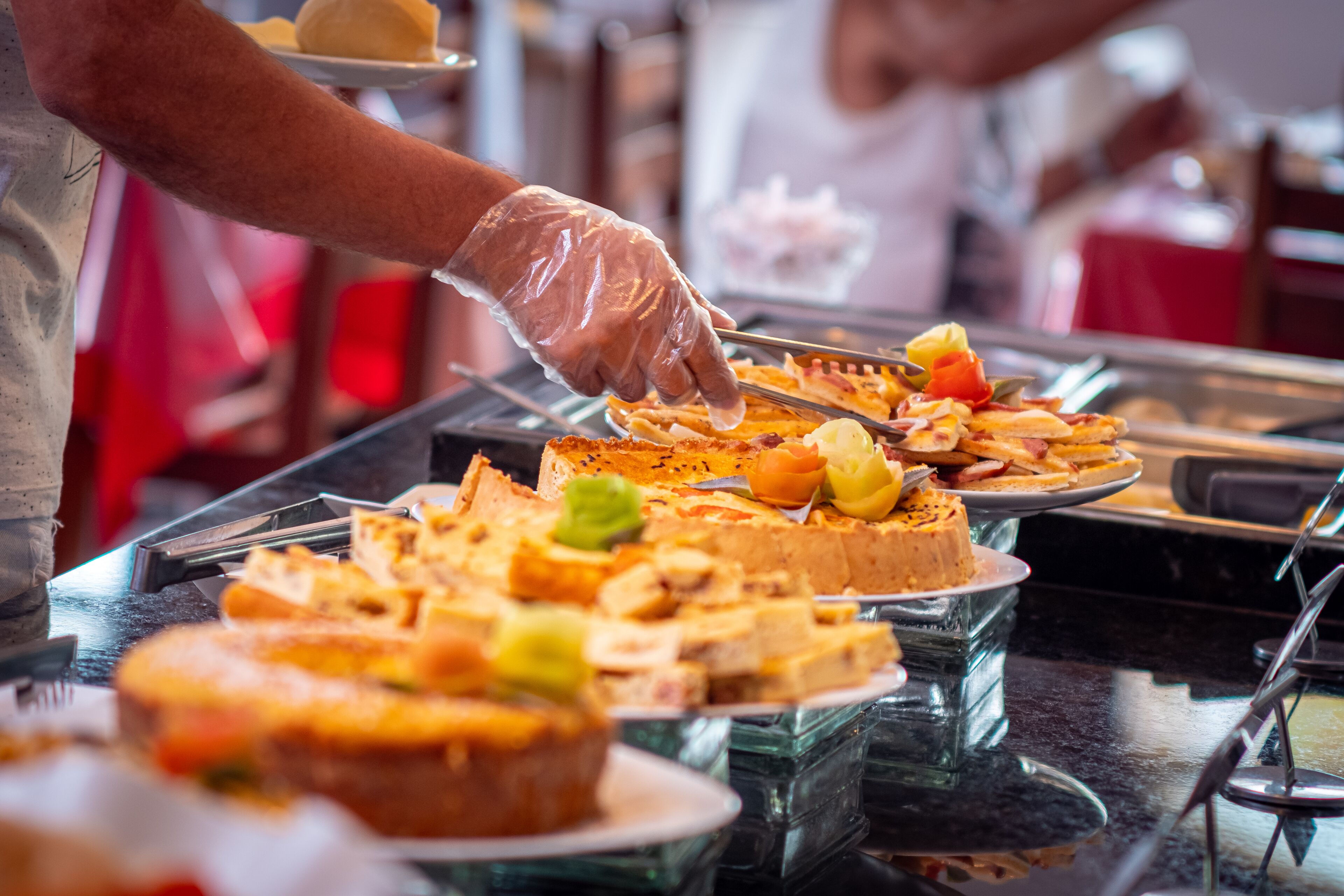 Buffet com diversos pratos, incluindo um bolo e uma torta, sendo servido por uma pessoa usando luvas.