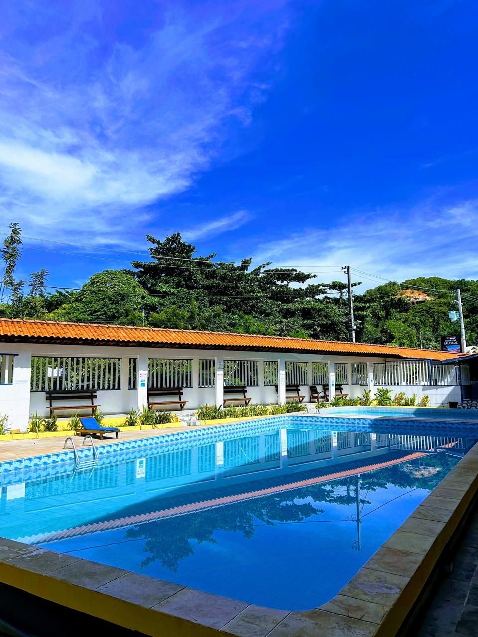 Piscina com deck revestido, bancos e área de estar coberta com telhado vermelho.