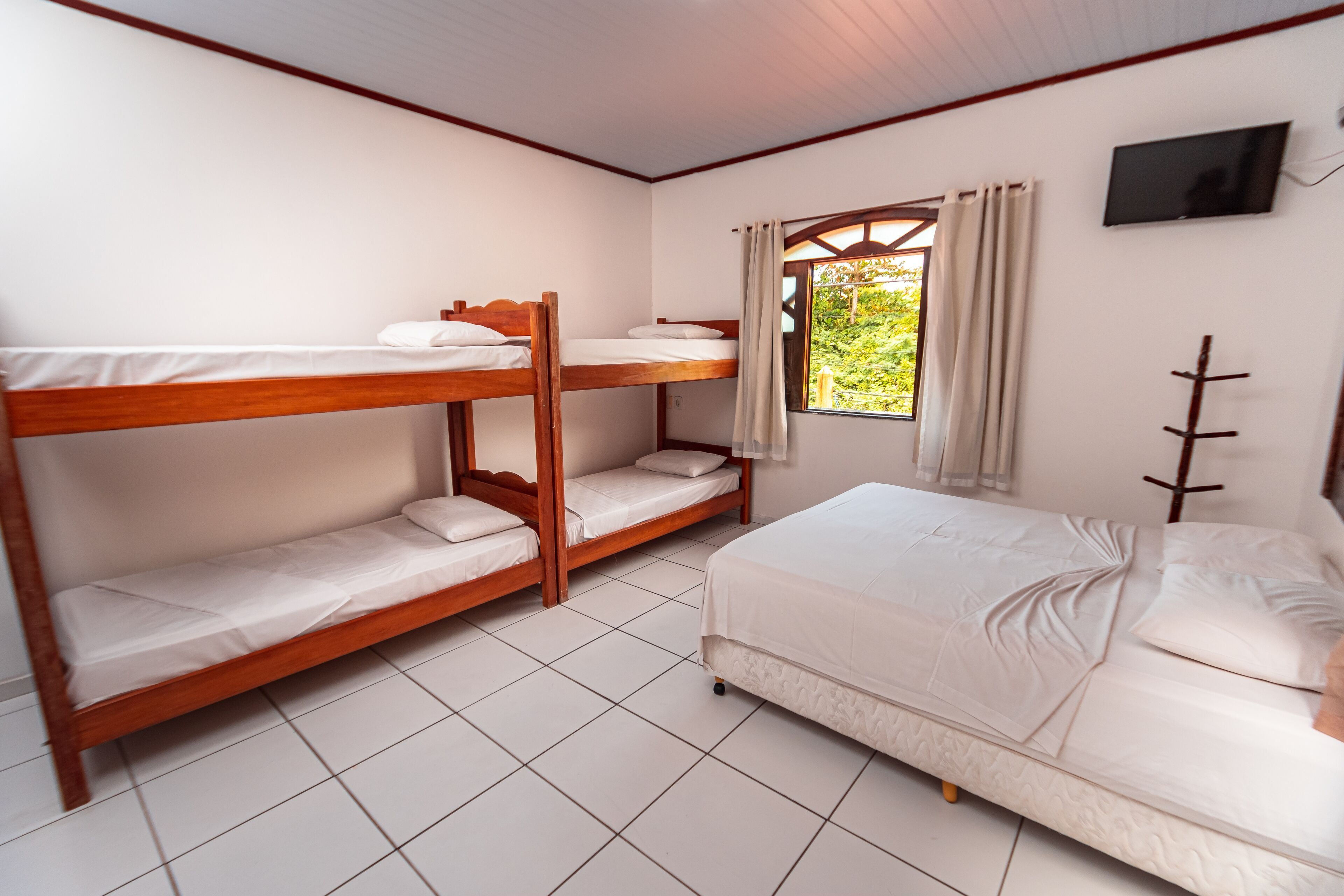 Una habitación con literas, una cama individual, un televisor en la pared y una ventana con cortinas.