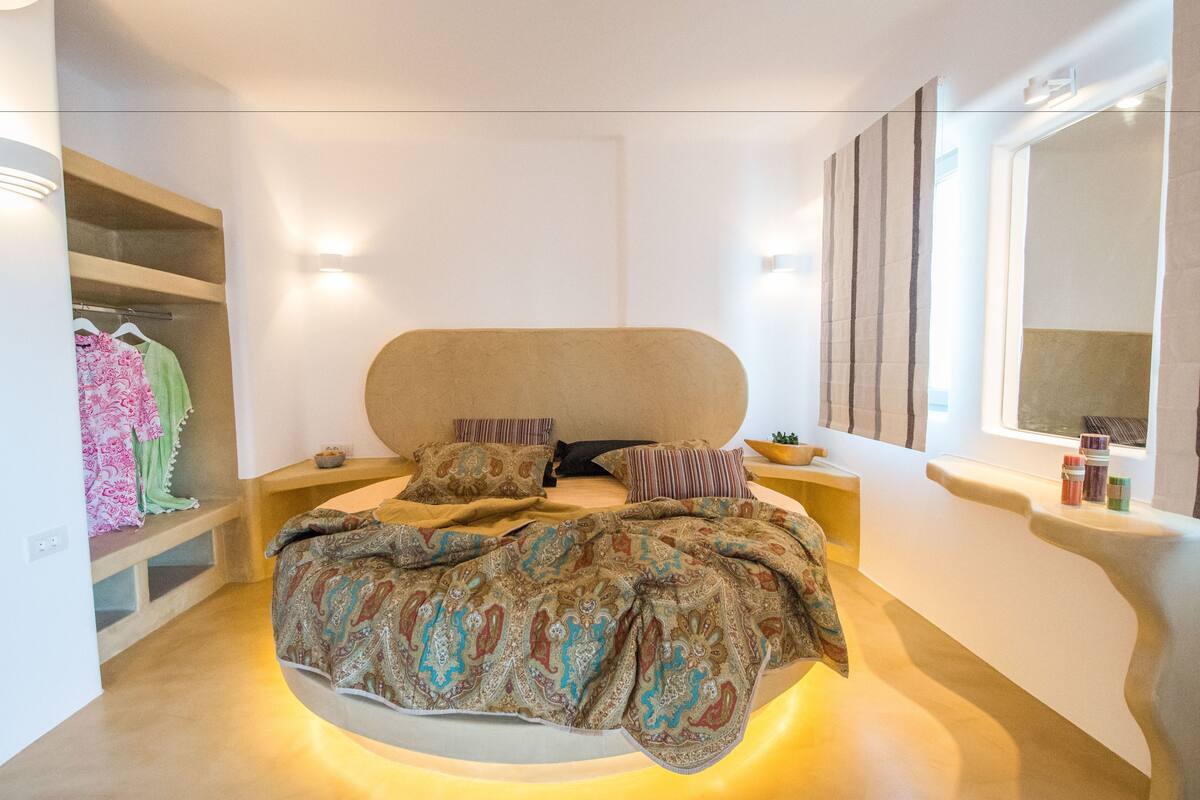 Un dormitorio moderno con una cama curvada, estanterías empotradas y un espejo grande.