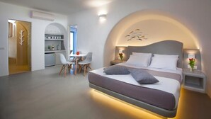 Une chambre d’hôtel moderne avec un grand lit, un bureau et une chaise. On y trouve également un coin cuisine avec un évier et une étagère où sont rangées des bouteilles.