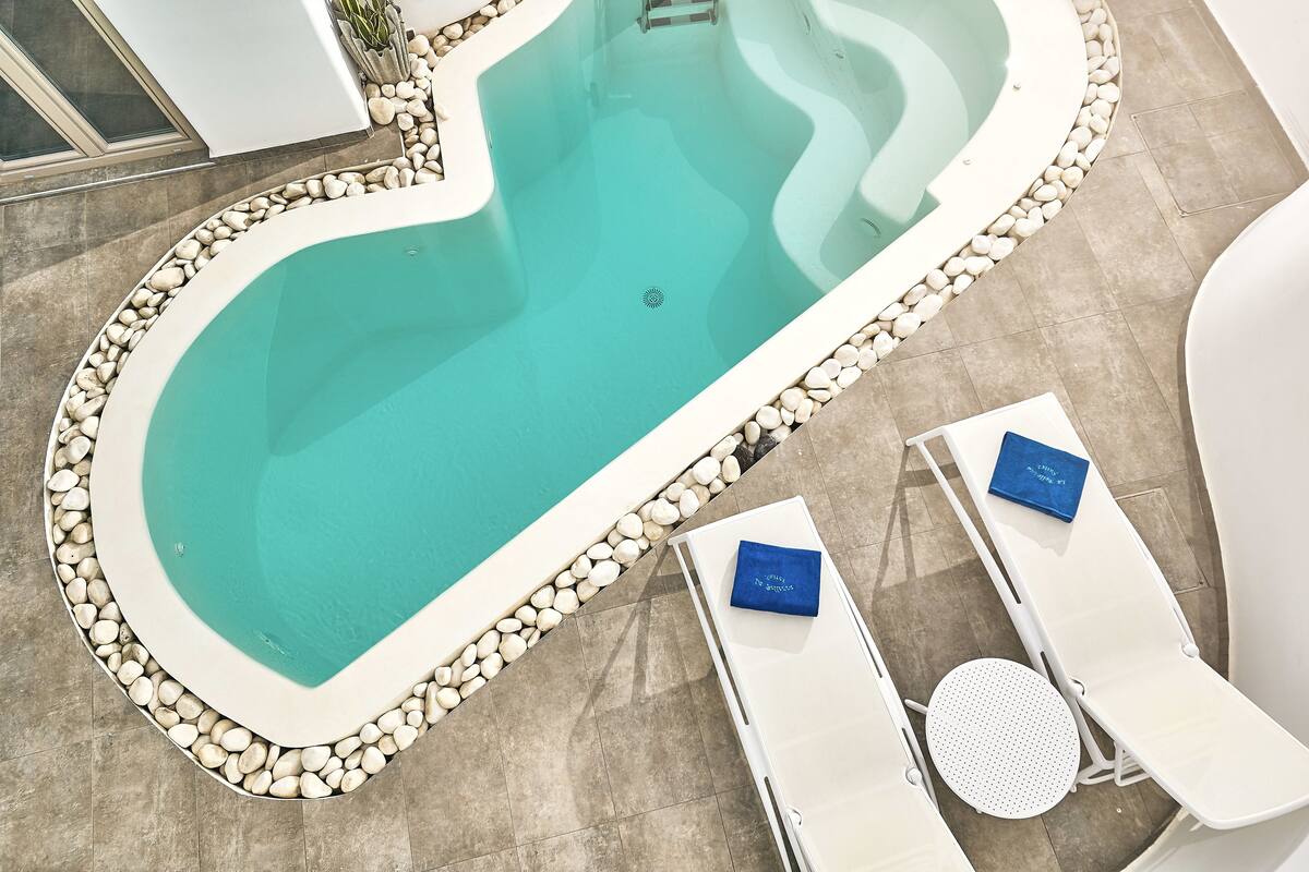 Una piscina con borde de guijarros, dos sillones de playa con toallas y una pequeña mesa redonda.