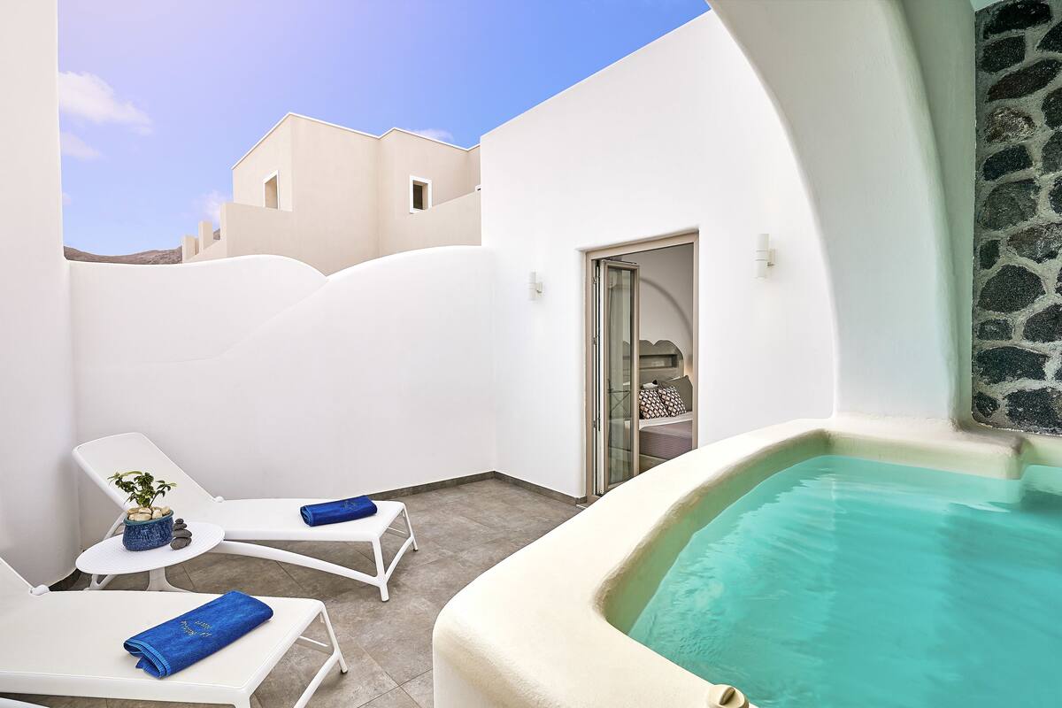 Un área de piscina moderna al aire libre con sillones de descanso blancos y una pared de piedra.