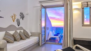 Une chambre avec un canapé, une table de chevet et une vue sur le balcon, avec le soleil couchant en toile de fond.