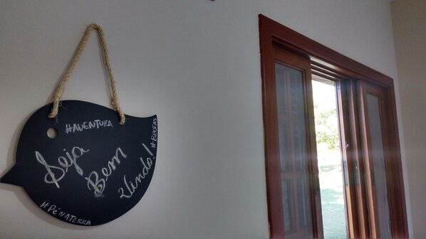 A wall-mounted sign with handwritten text and a rope handle. - Pousada Pé na Terra (Brotas)