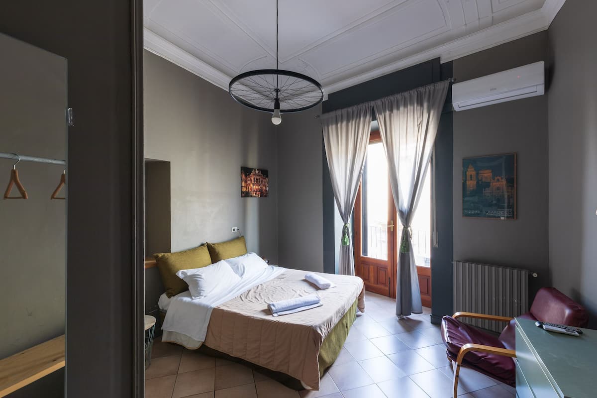 Un dormitorio con cama, escritorio, silla, radiador y ventana con cortinas.