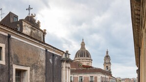 A narrow street with buildings on either side, a white van parked on the street, and a person walking in the distance. - Terrazza Santa Chiara (Catania)